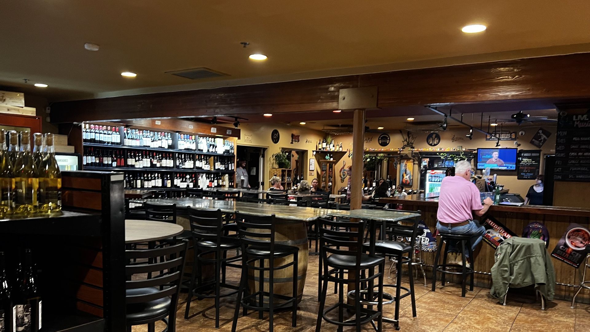 Bar interior with seating, bottles of wine on shelves, and a person sitting at the bar.