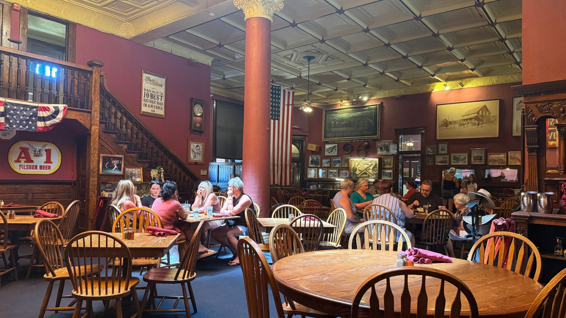 Interior of a restaurant. People seated at tables. Red walls, wooden furniture, and historical decor.
