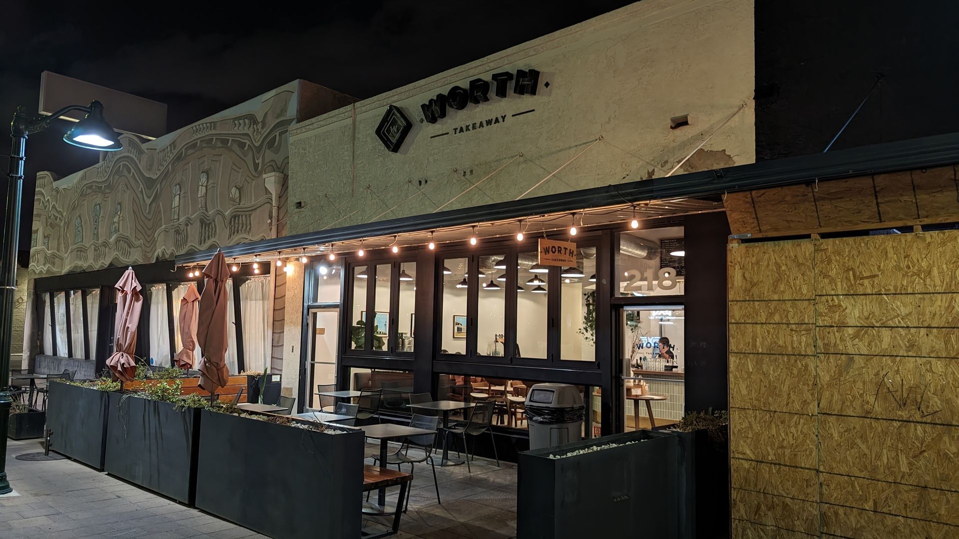 Exterior of a restaurant at night with string lights, outdoor seating, and signage.