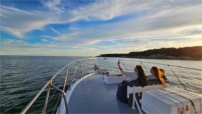 Two people take a selfie on a boat, sailing on the ocean under a blue sky.