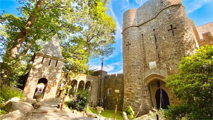 Stone castle with arched entryways, tall tower, and green trees under a blue sky.