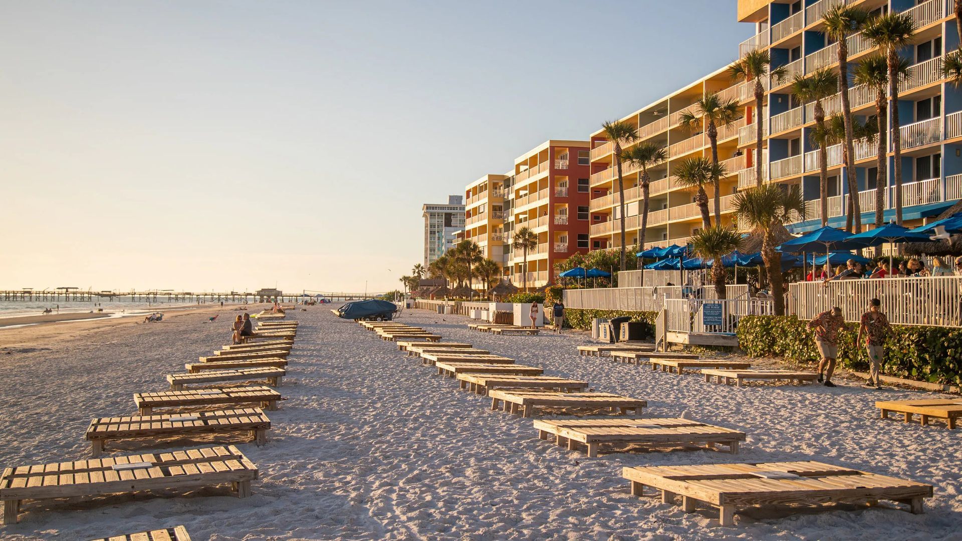 Beach scene with rows of wooden beach chairs in front of a colorful hotel at sunset.