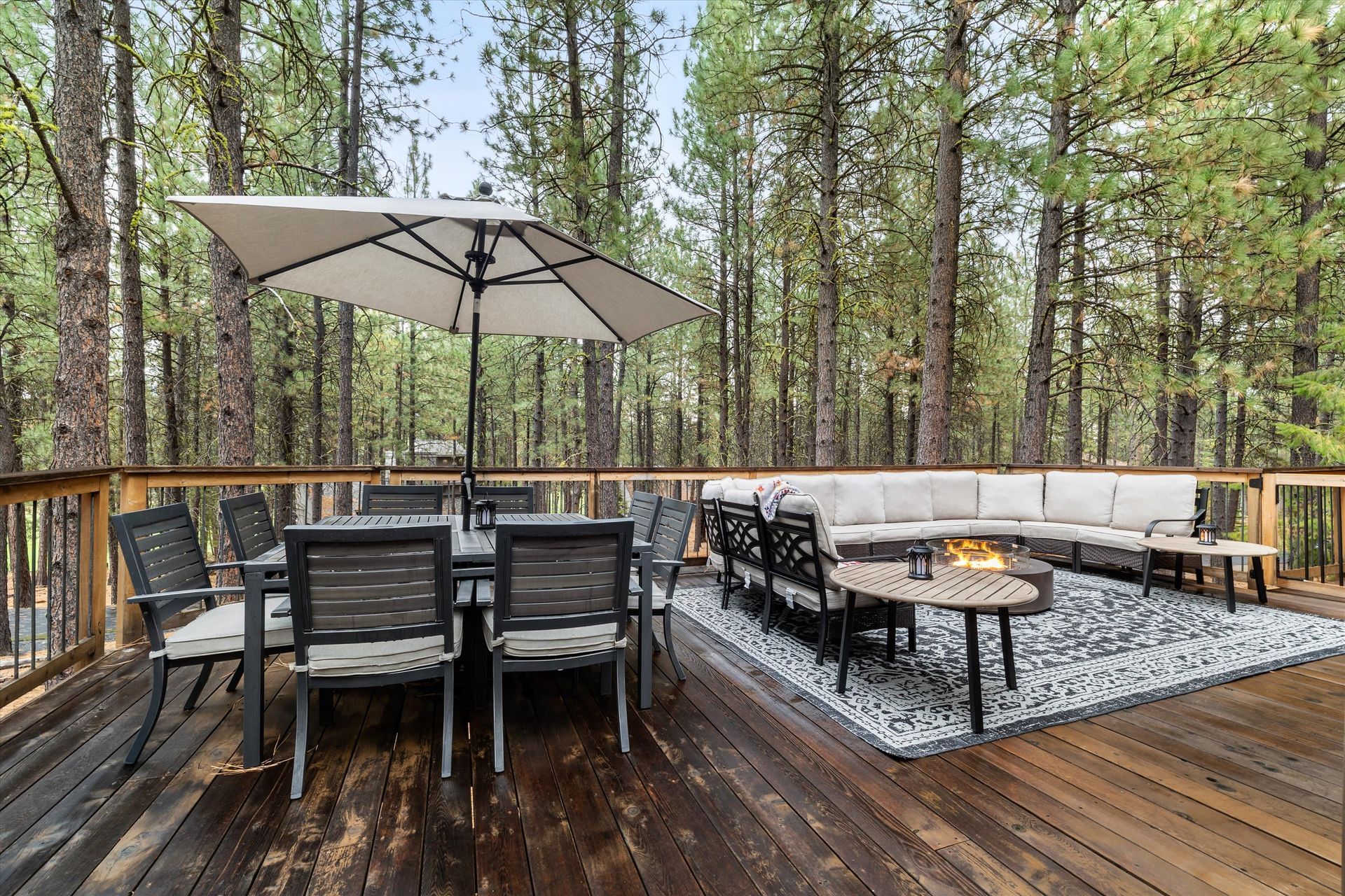 Wooden deck with outdoor dining set, lounge seating, and umbrella in a pine forest backyard
