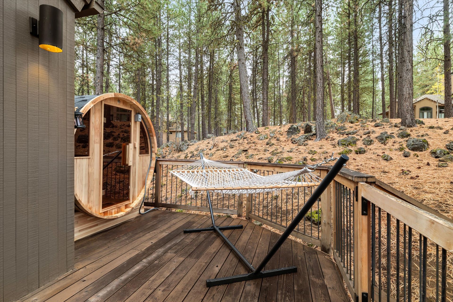 Wooden deck with a hanging chair and sauna barrel overlooking a pine forest