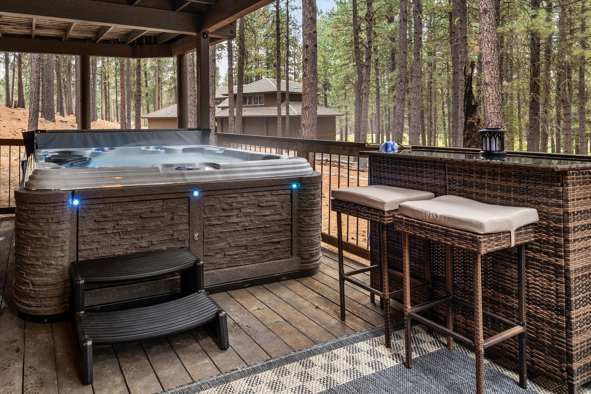 Wooden deck with a covered hot tub and wicker seating in a pine forest resort setting