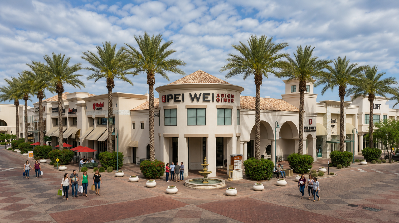 Outdoor plaza at Hotel del Vey with palm trees, arched entrance, and people walking around