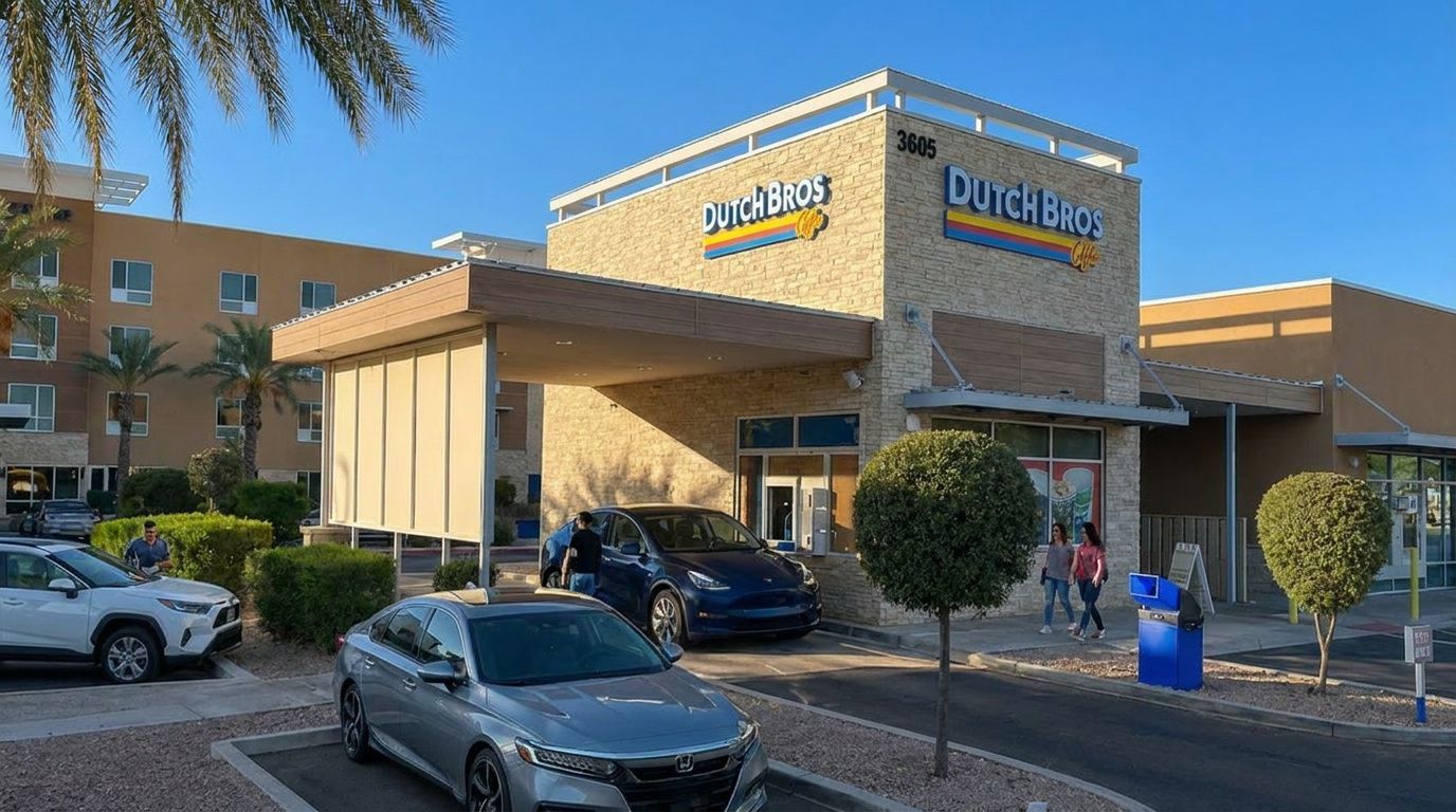 Dutch Bros coffee drive-thru with cars waiting under a yellow canopy at a sunny shopping center
