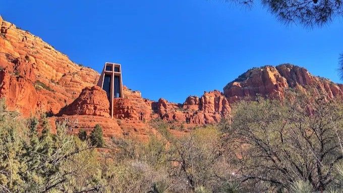 Chapel of the Holy Cross built into red rock mountains against a clear blue sky.
