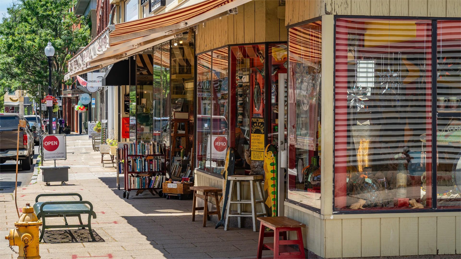 Street with shops, sidewalk, and parked cars on a sunny day.
