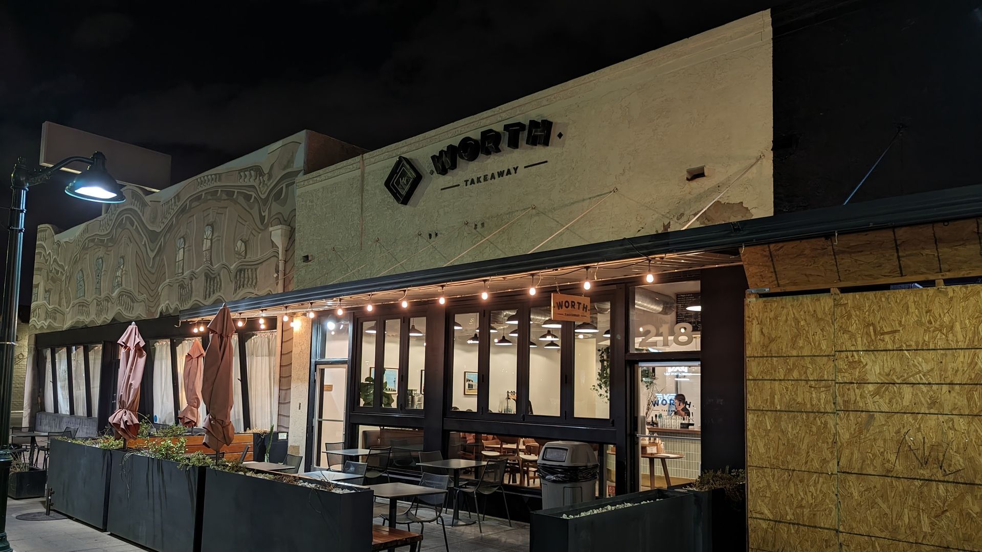 Exterior view of a restaurant, lit at night with string lights and outdoor seating; sign reads 