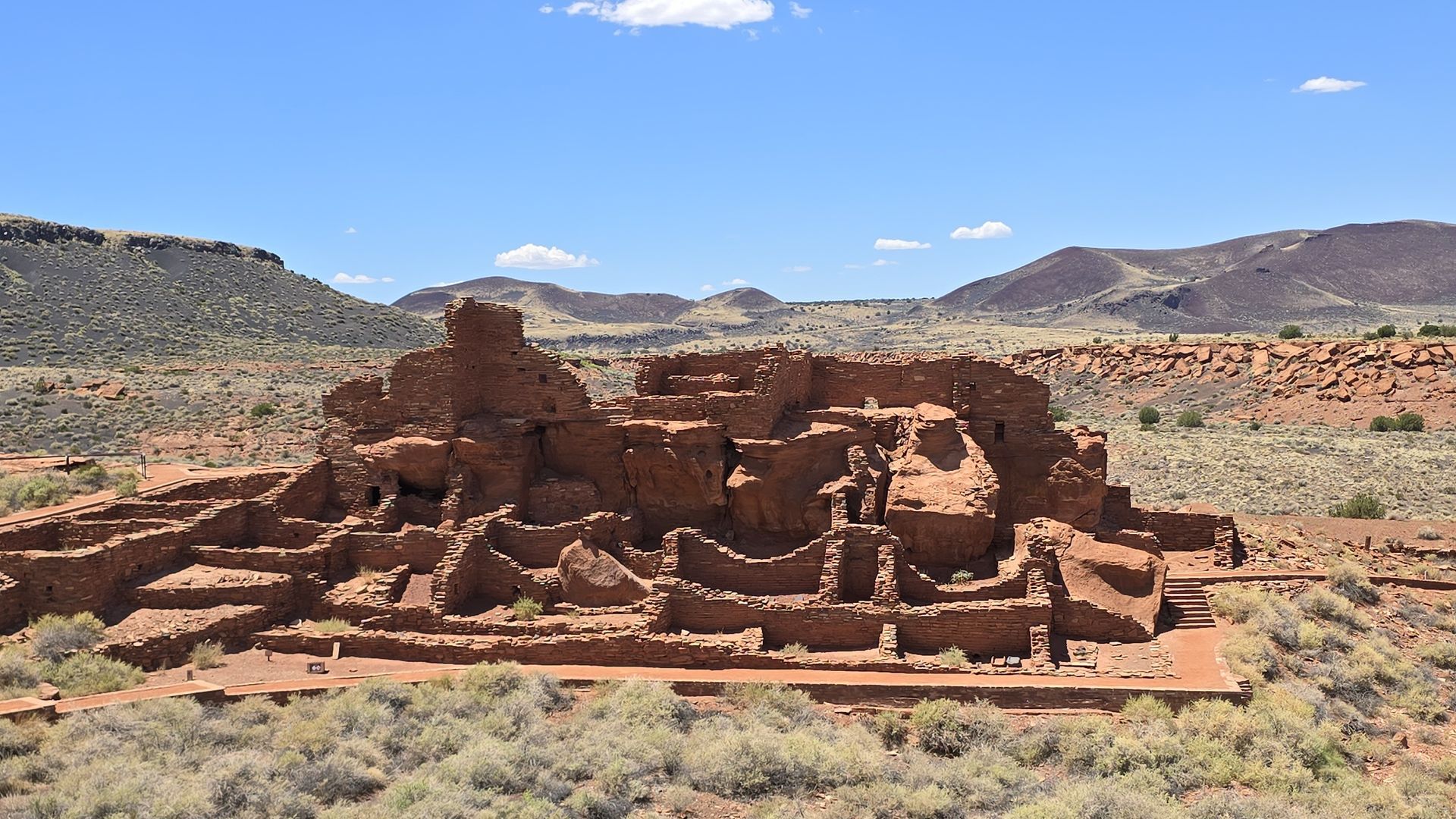 Ruins of a large, red-stone structure in a desert landscape under a clear blue sky.