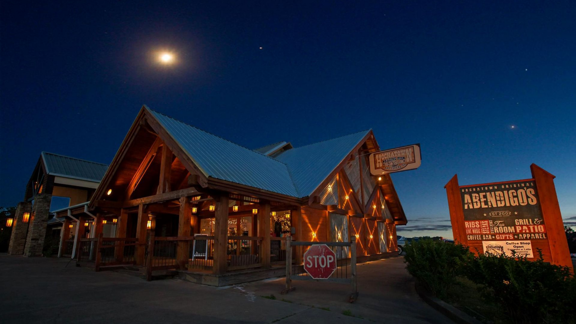 Night shot of Averill's restaurant with outdoor lights, a sign, and a stop sign. Moon and stars in the night sky.