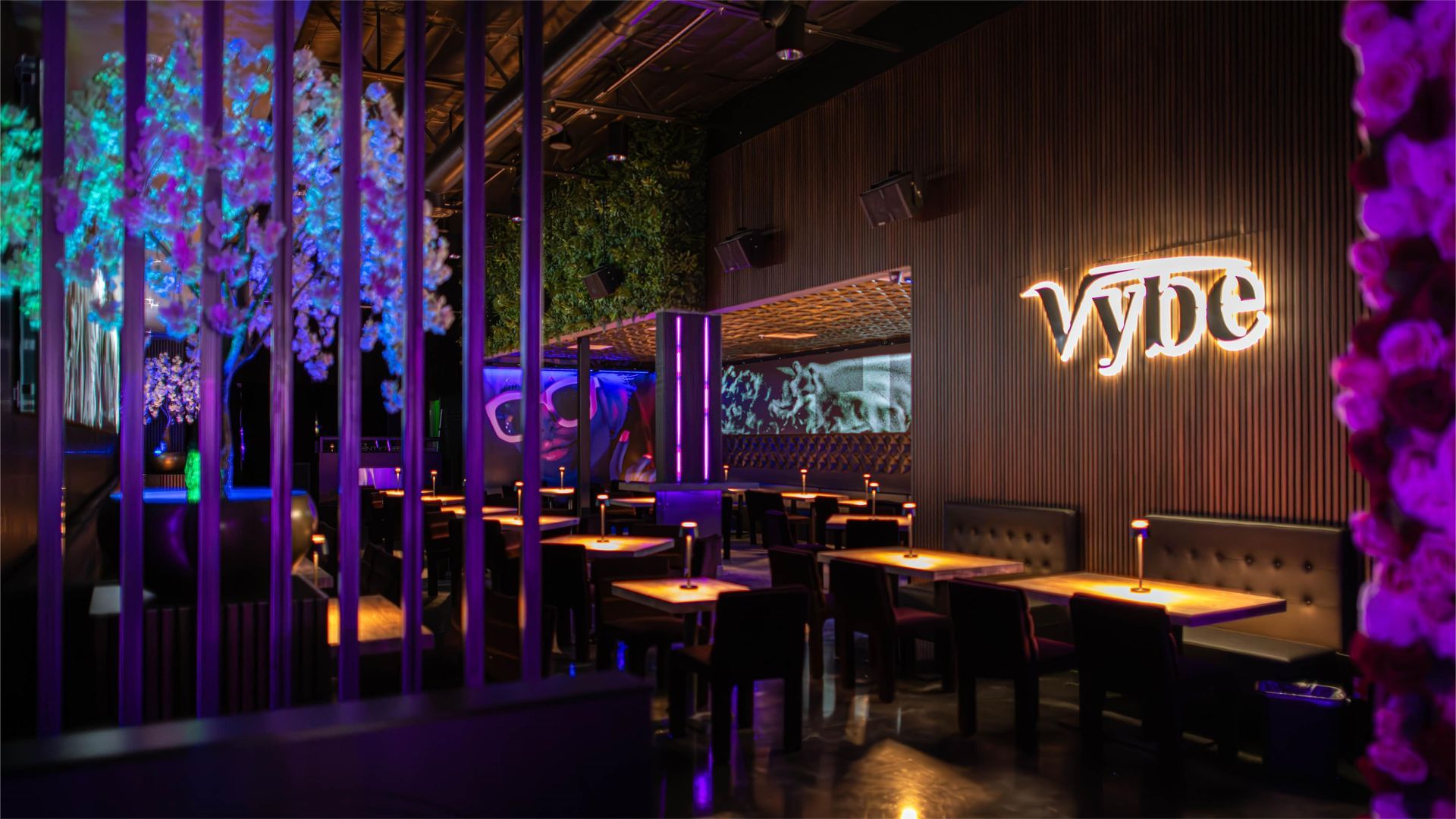 Interior of a dimly lit restaurant or bar, featuring tables, seating, and decorative neon signage.