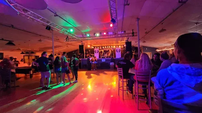 People at a dance club with stage, lights, and red and green floor lighting.