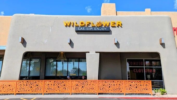 Wildflower restaurant exterior with yellow signage, a patterned orange fence, and large windows.