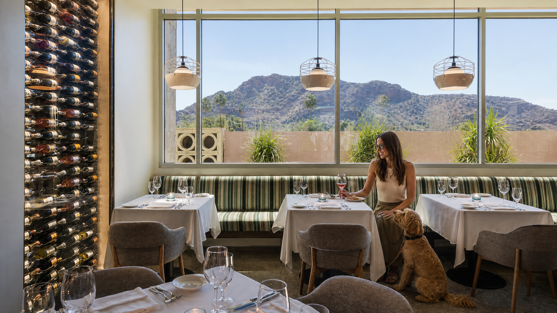 Elegant restaurant interior with set tables and a woman seated by floor-to-ceiling windows overlooking mountains