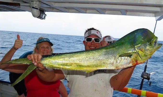 Man and woman holding large, colorful mahi-mahi fish on a boat; smiling with thumbs up.