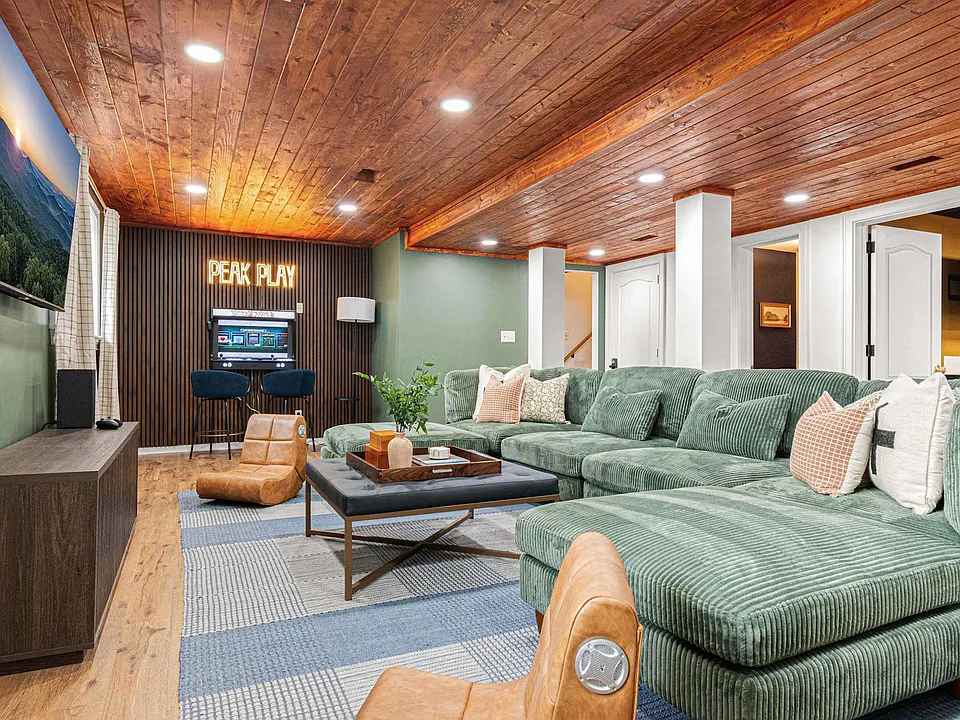 Green sectional sofa in a wood-paneled living room with a coffee table and fireplace, lit by recessed lights