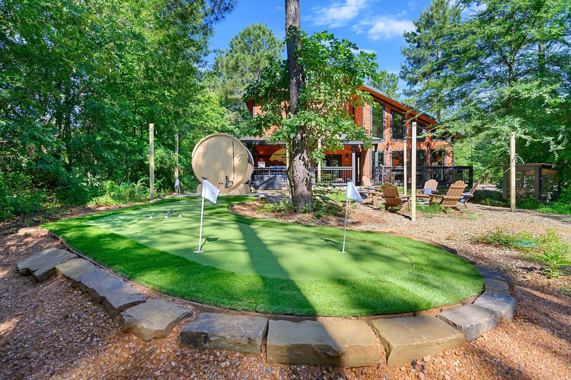 Backyard putting green beside a brick house, with a satellite dish and trees in bright sunlight