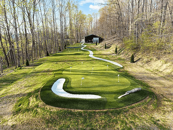 Curving miniature golf green with white water hazards, surrounded by trees, leading to a small shelter