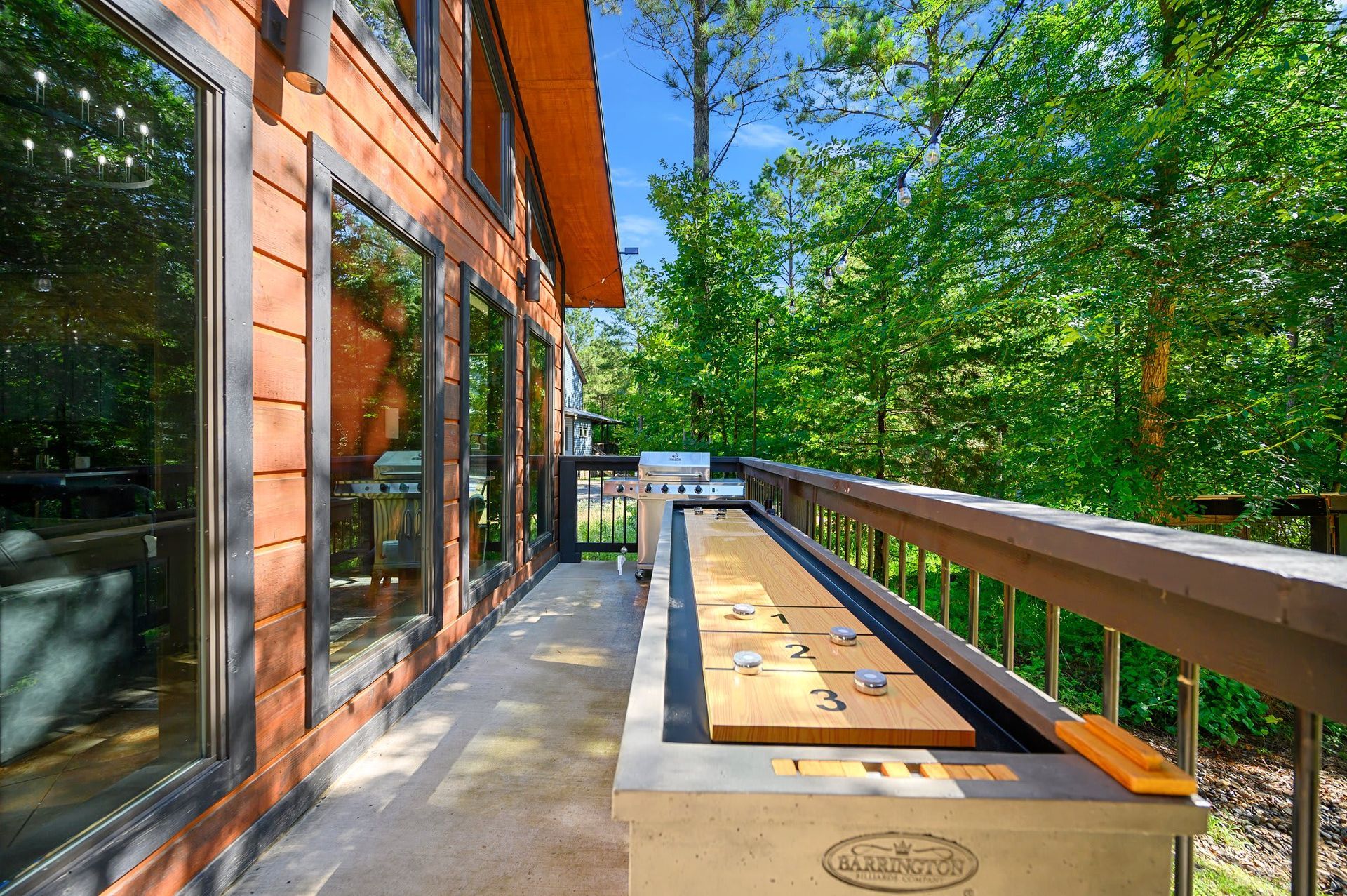 Modern deck with wooden bench, glass windows, and green trees in sunlight