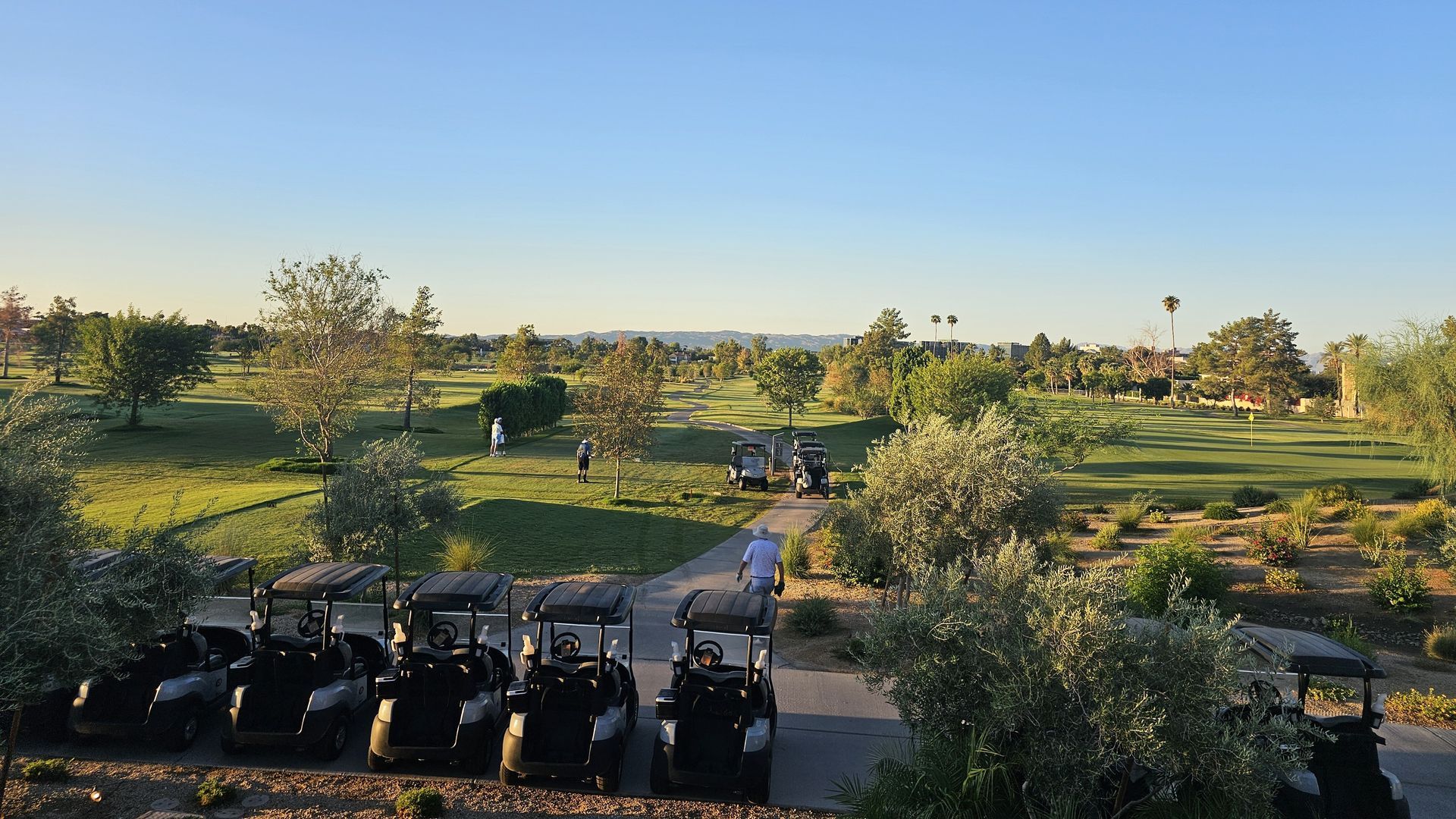 Golf course with carts in the foreground. People playing golf on a sunny day.