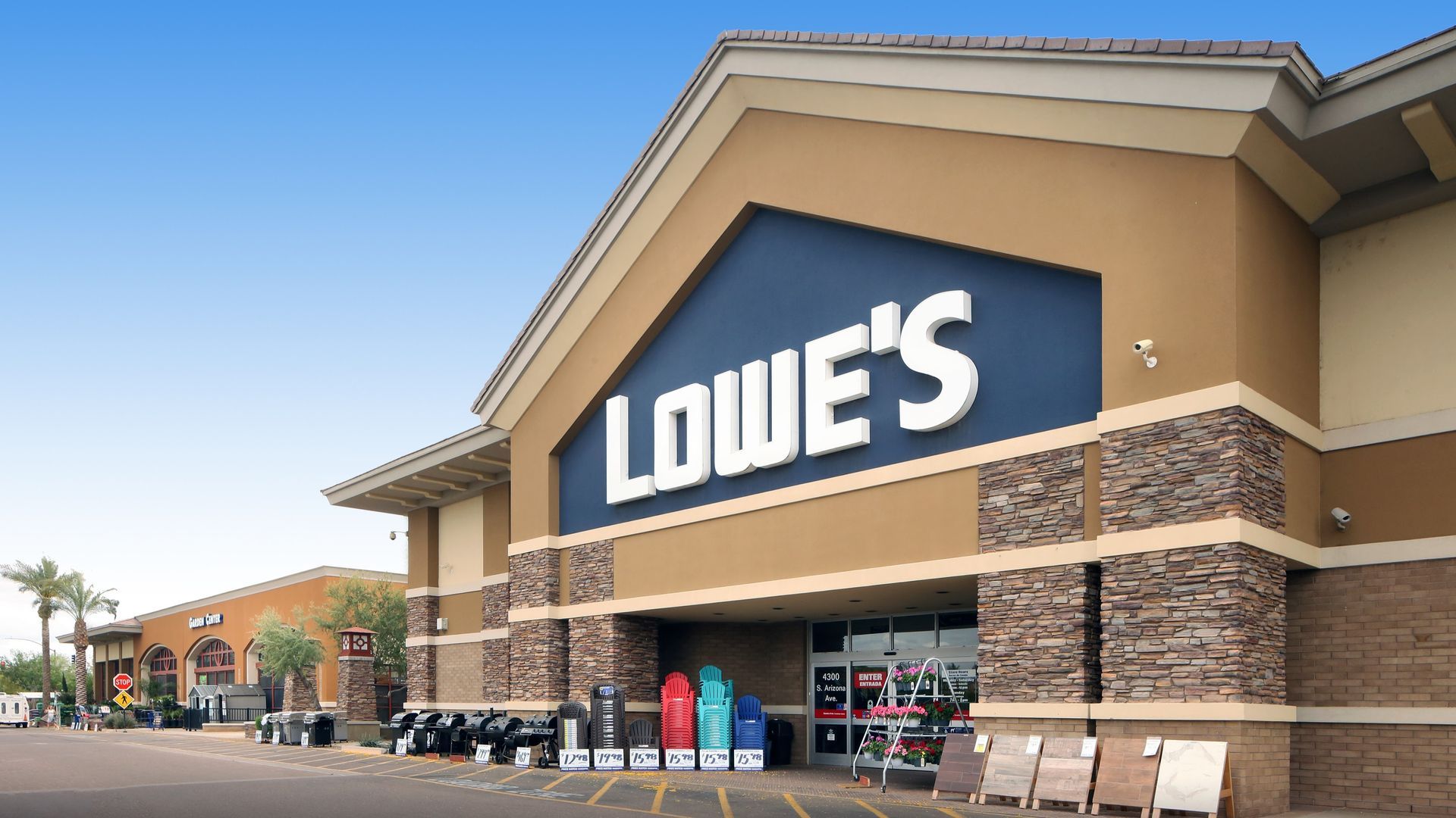Lowes store exterior, tan and brown building, blue sky, parking lot, entrance visible, sign with company logo.