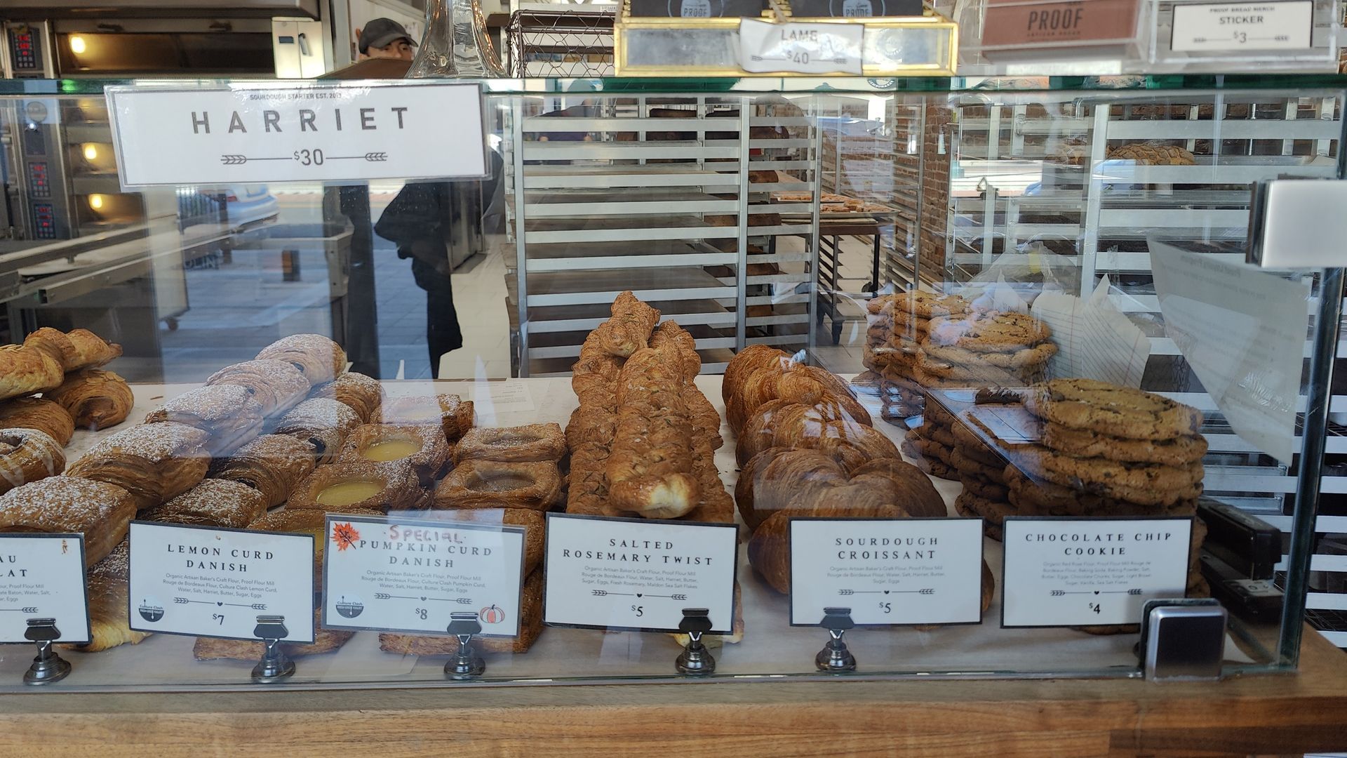 Bakery display case with various pastries, including croissants and cookies, with signs.