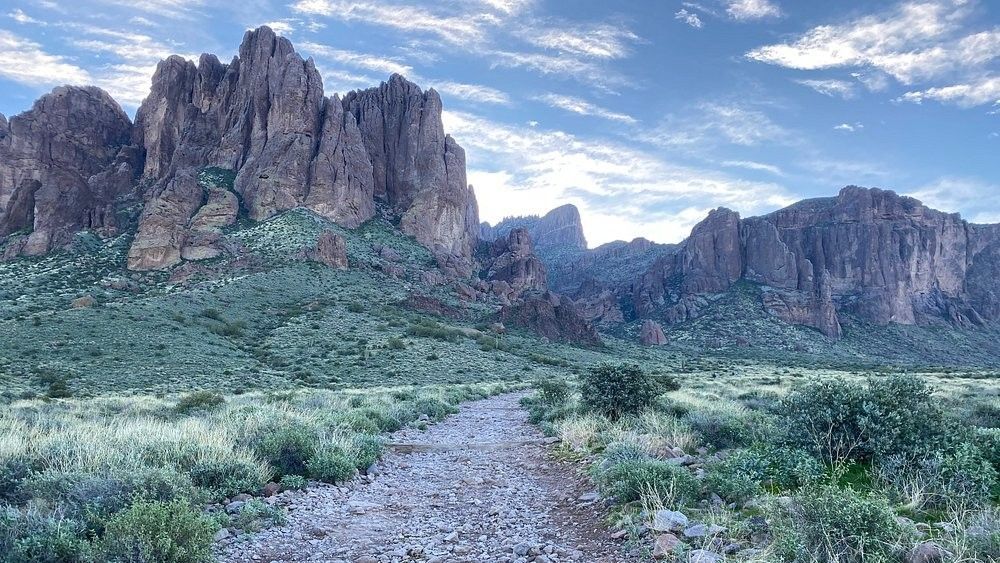 Rocky trail through desert landscape toward rugged mountains under a blue sky.