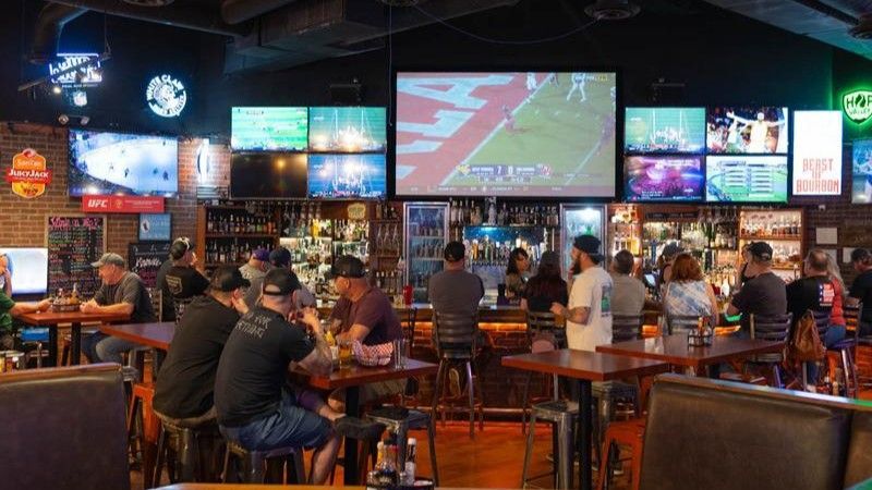 A crowded sports bar with multiple TVs showing sports games. People sit at tables and the bar.