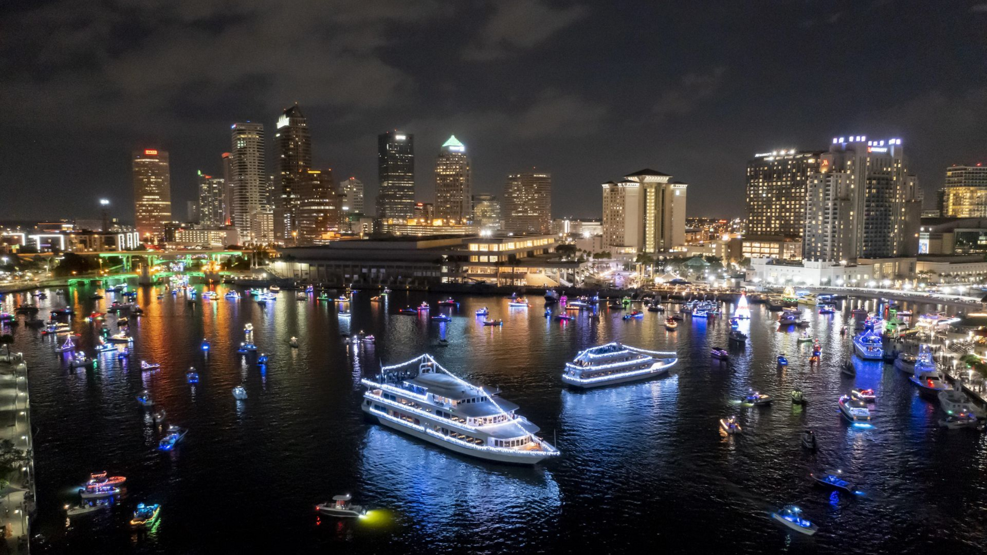 Night scene of Tampa Bay, Florida, with boats lit up, skyline in the background.