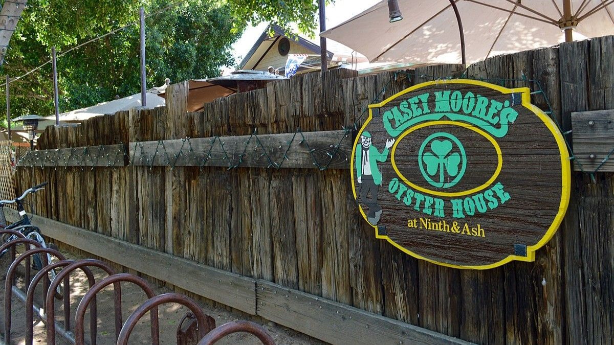 Casey Moore's Oyster House sign on a weathered wooden fence, featuring a shamrock graphic.