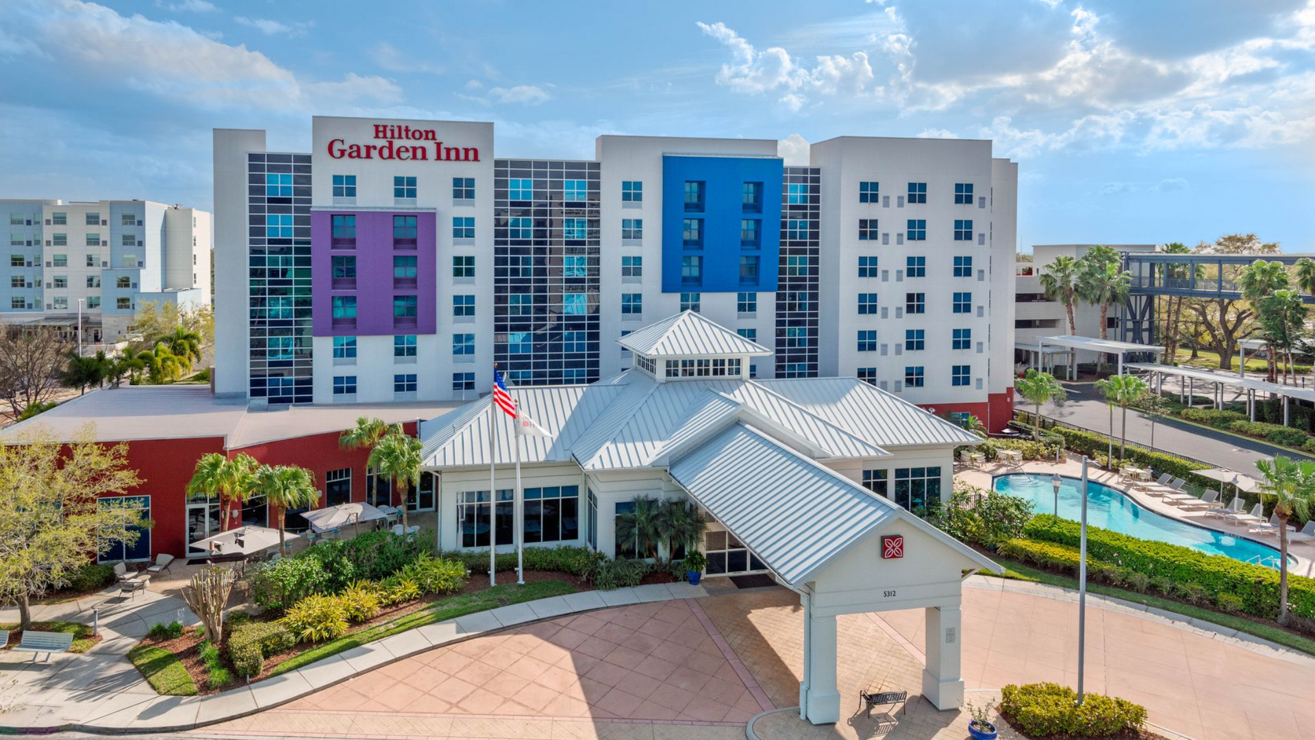 Hilton Garden Inn hotel exterior with a pool, colorful accents, and blue sky.