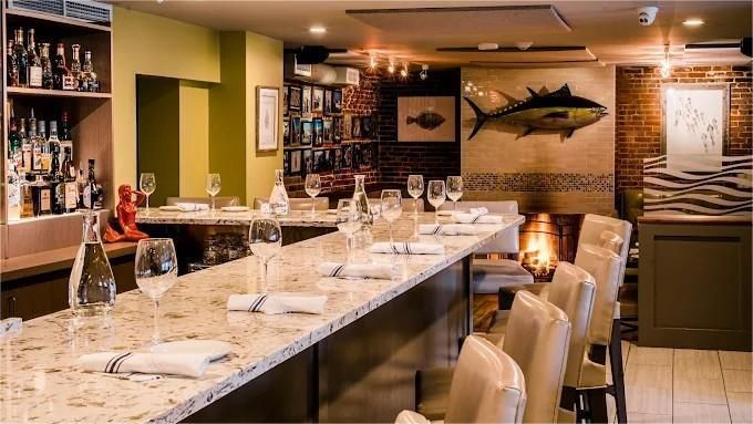 Restaurant bar with white countertop, wine glasses, and a tuna fish art piece.