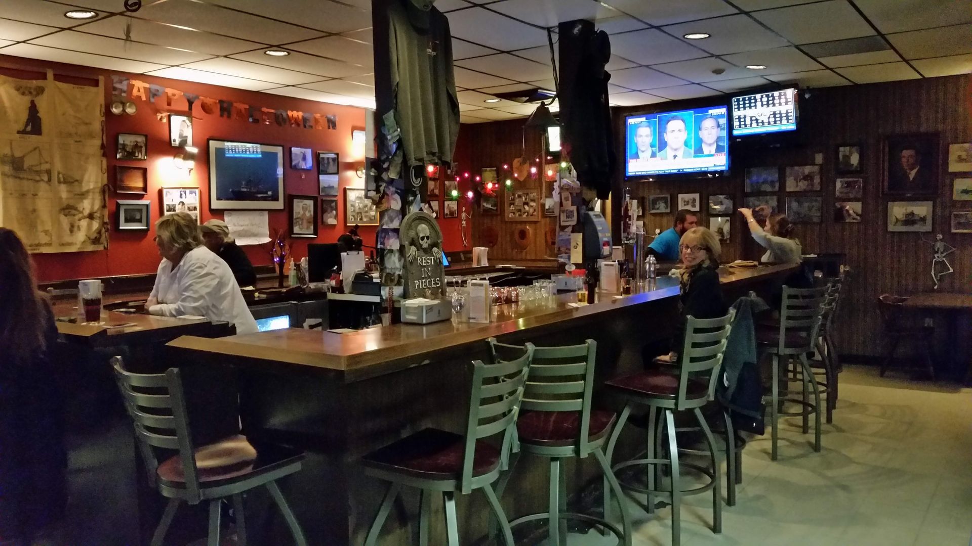 Interior of a bar with people seated at the bar and watching a TV.
