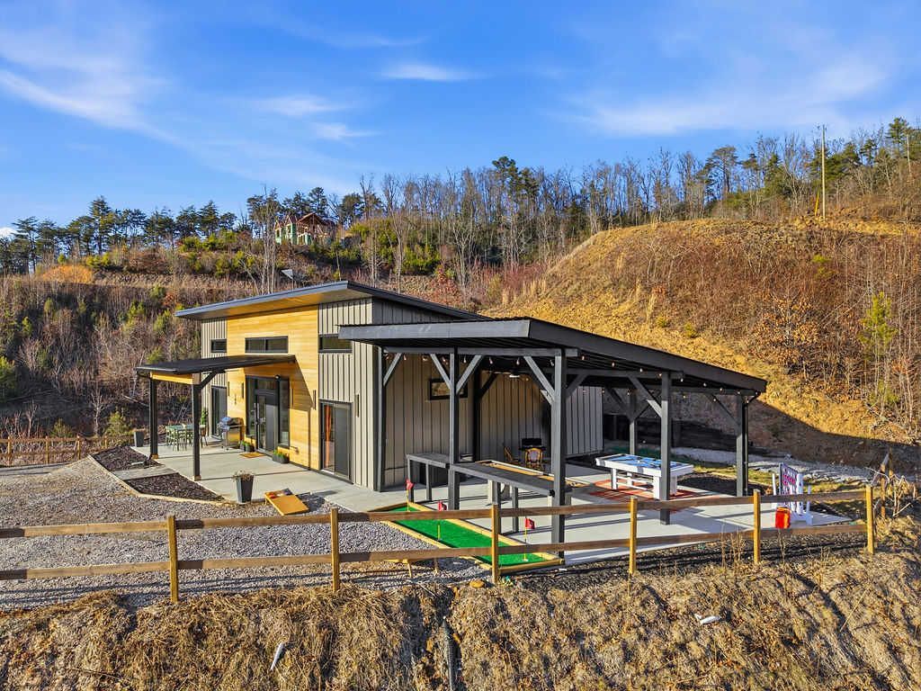 Small modern house with a covered patio on a gravel lot, surrounded by dry hills and trees.