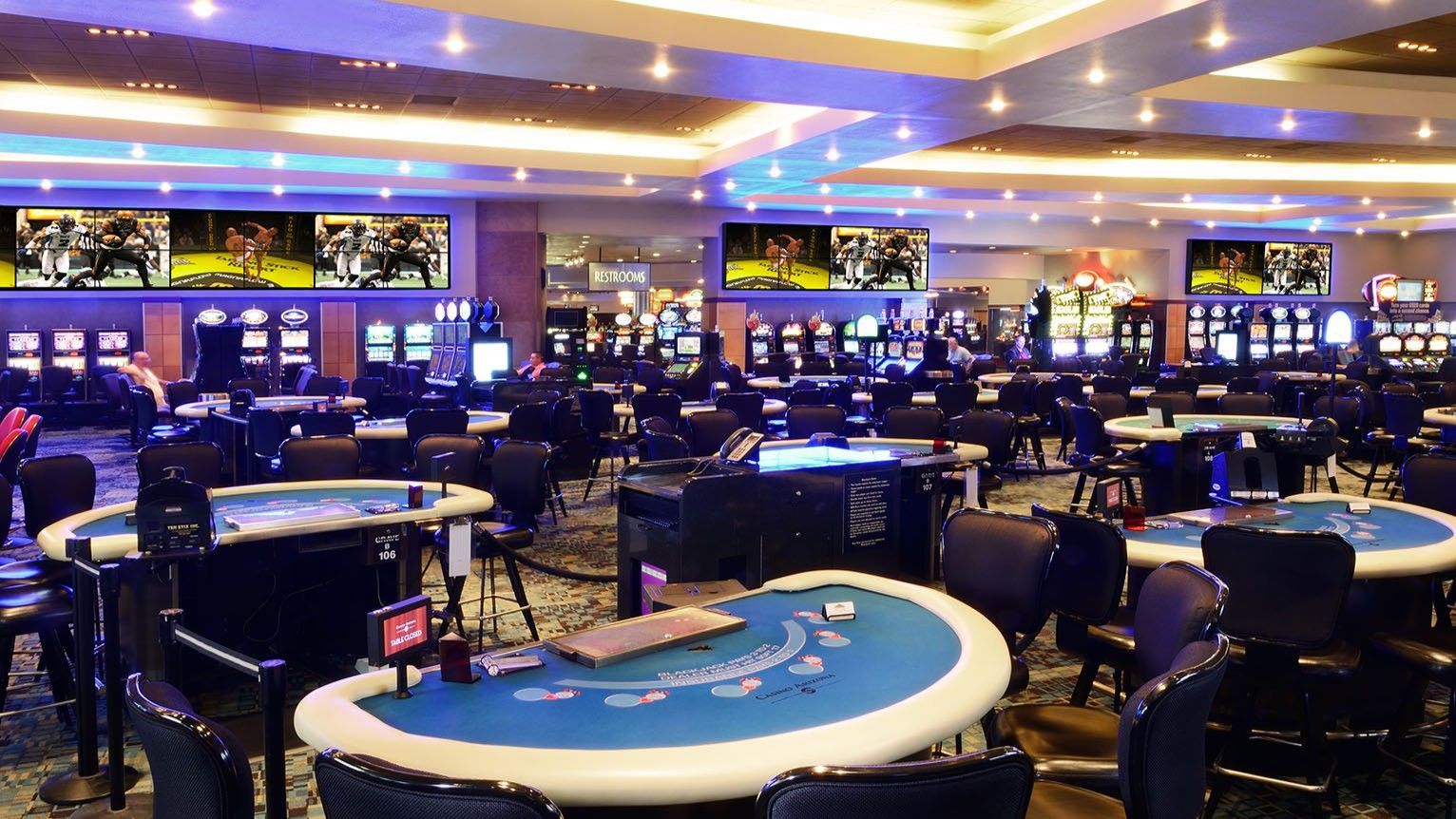 Casino interior with poker tables, slot machines, and TVs displaying sports.