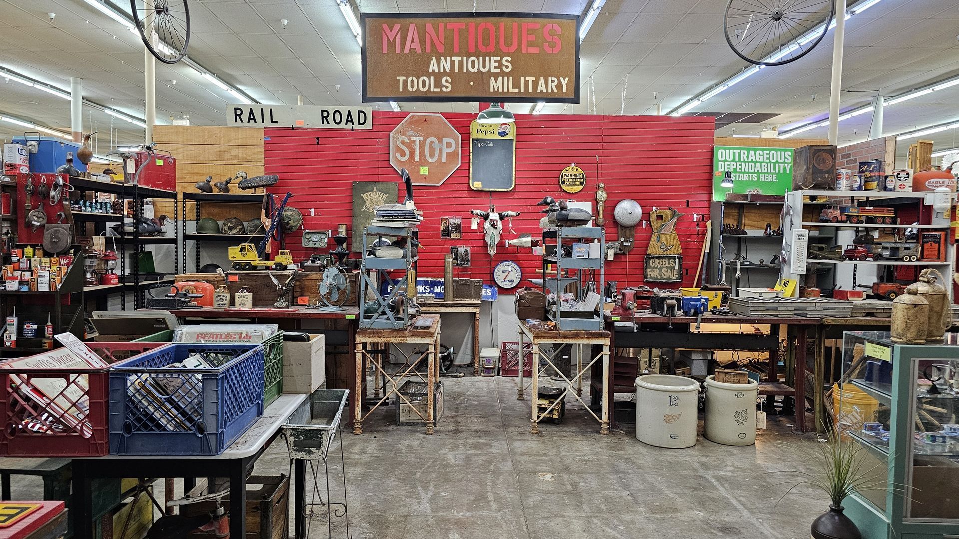 Antique shop interior with red backdrop, tools, signs, and assorted vintage items for sale.