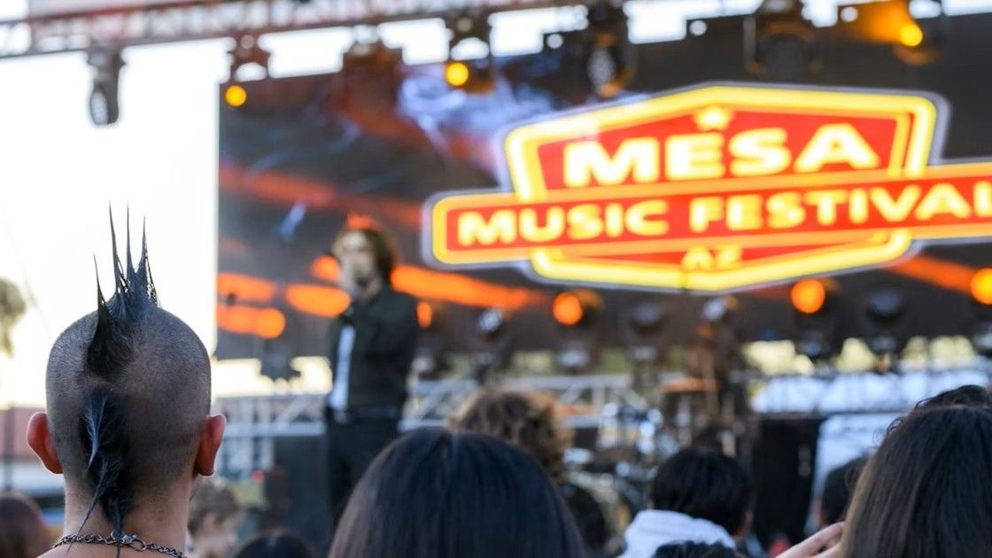 Person with mohawk at the Mesa Music Festival. Stage and crowd in background, event logo visible.