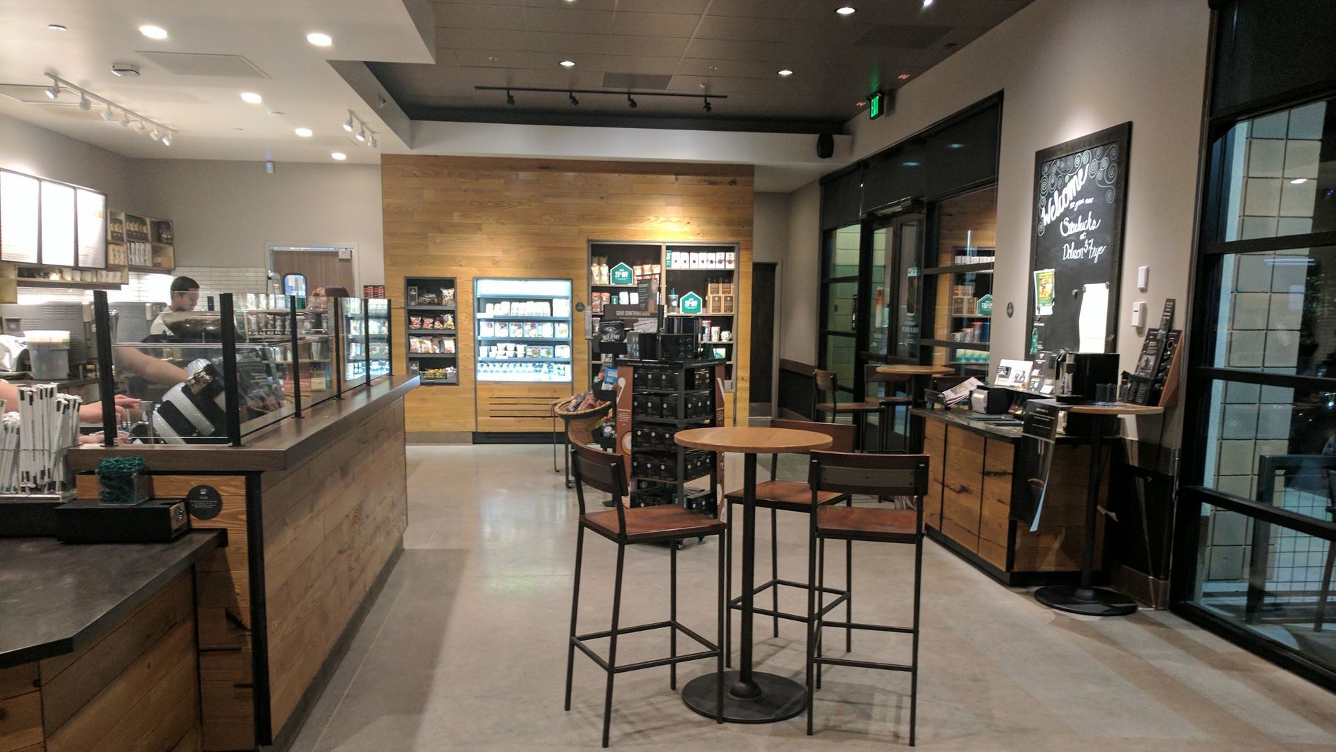 Interior view of a Starbucks cafe, featuring a counter, tables, shelves with snacks, and a barista.