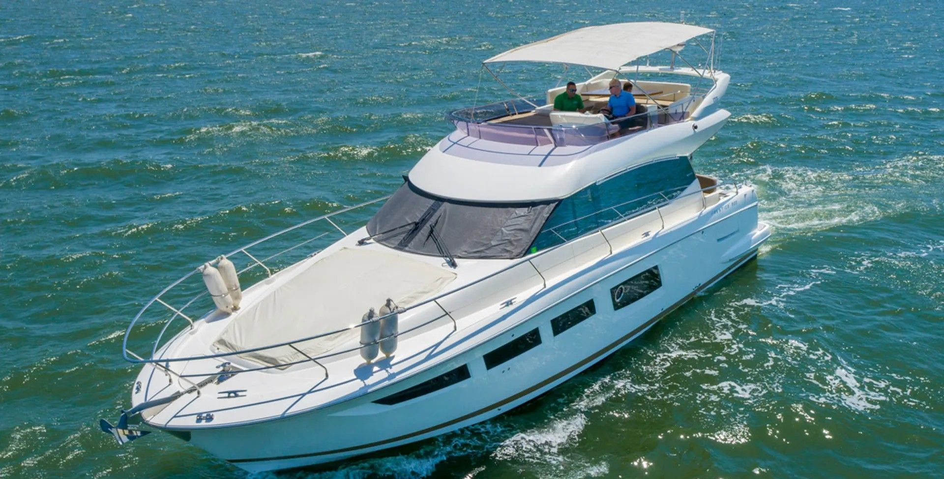 White motor yacht cruising on blue water, a person on the upper deck under a canopy.