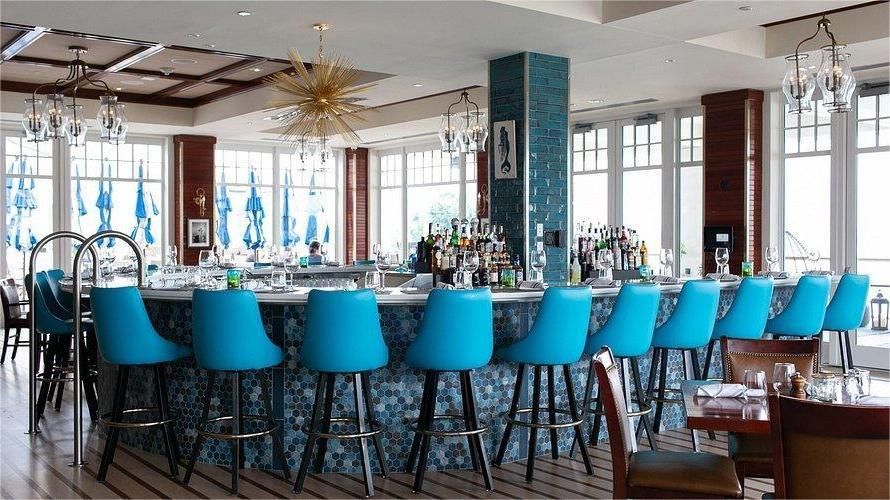 Bar with blue stools and mosaic tile. Bright, airy interior with large windows.