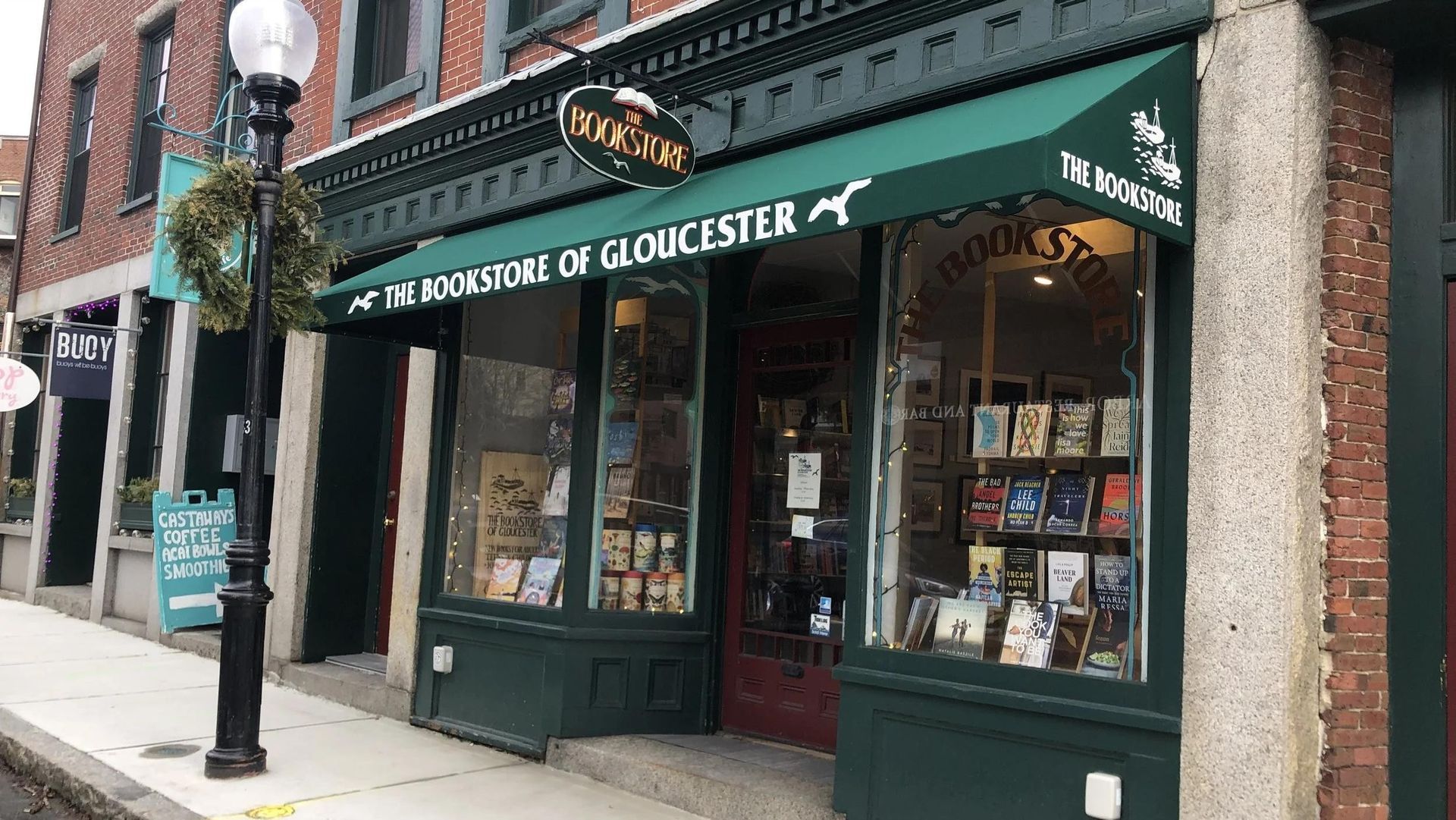 The Bookstore of Gloucester with green awning and a wreath, storefront on a brick building.