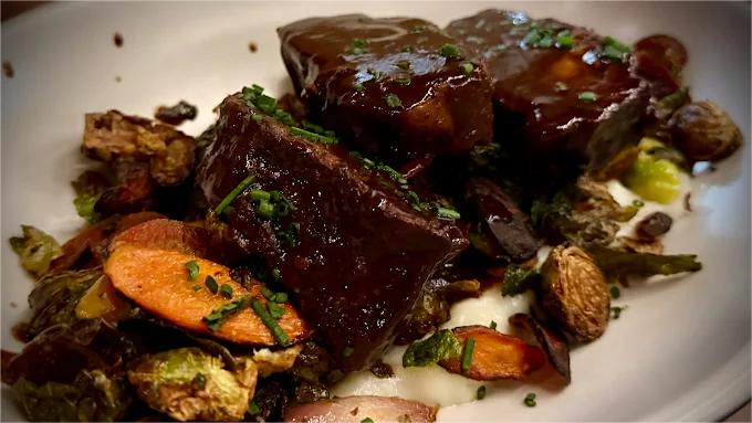 Braised short ribs with vegetables on a plate, dark brown sauce, overhead shot.