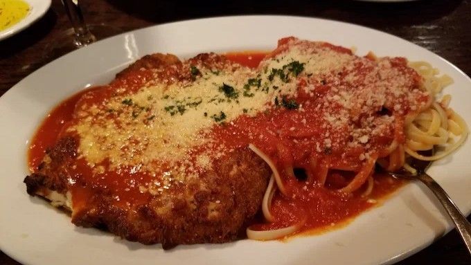 Chicken parmigiana with spaghetti and tomato sauce, on a white plate.