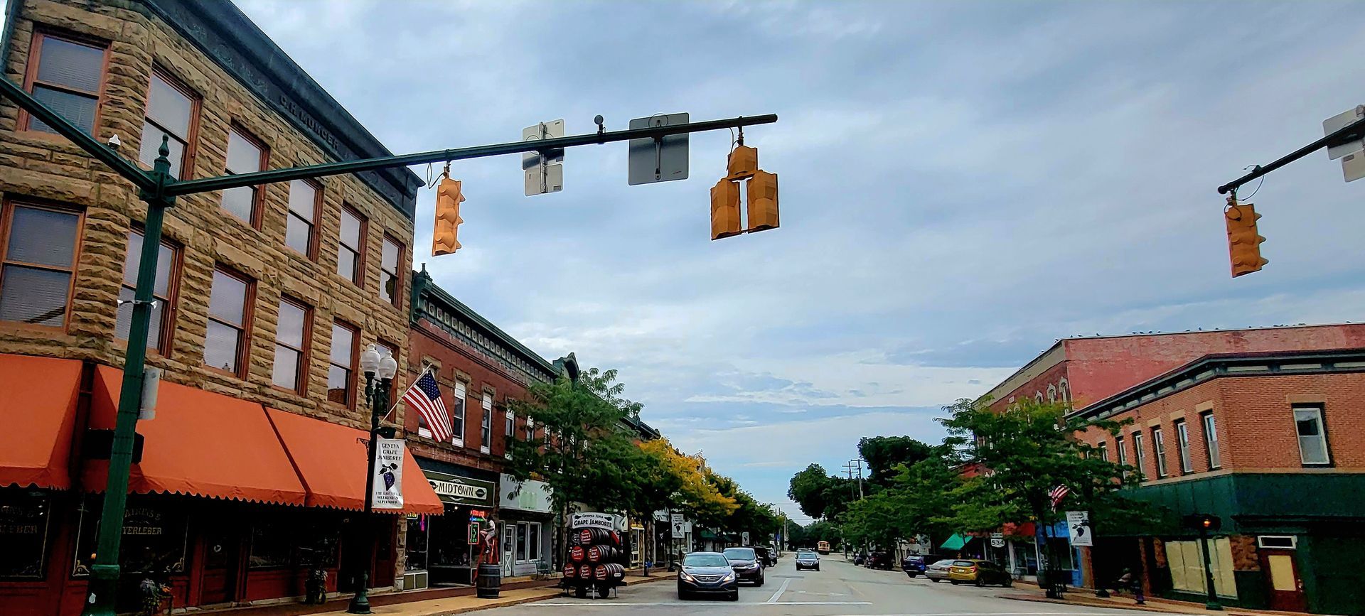 Street scene of brick buildings and traffic lights. Cars on the road, cloudy sky overhead.