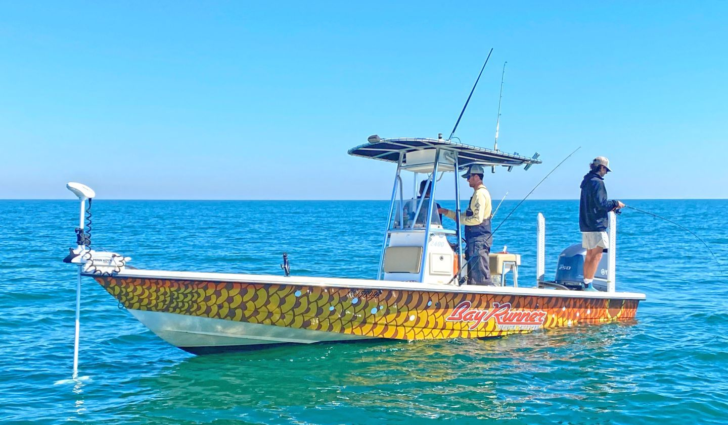 Boat with two people fishing on blue water under a clear sky.