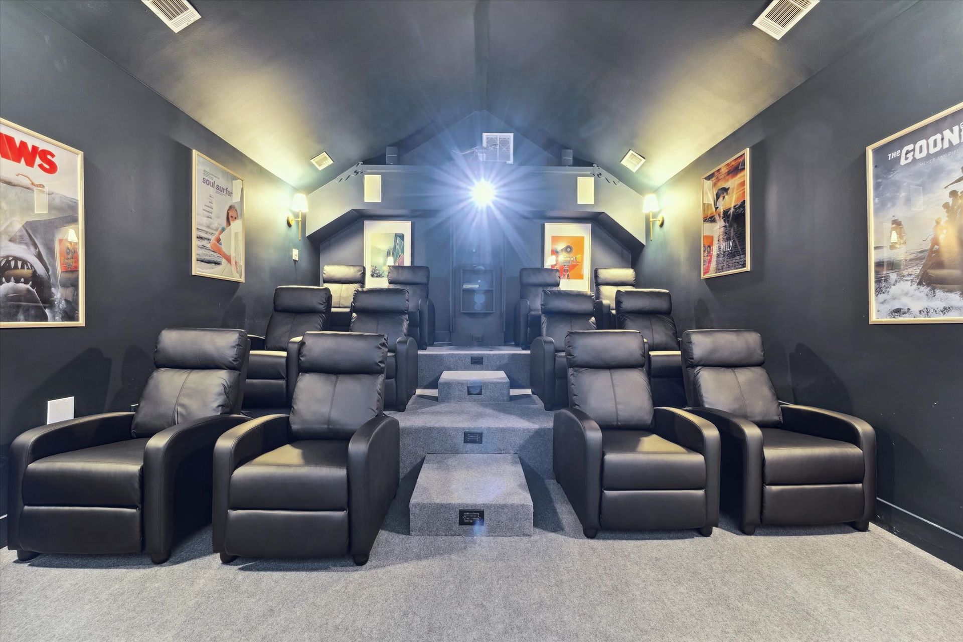 Home theater with rows of black recliners, gray carpet, and movie posters on dark walls