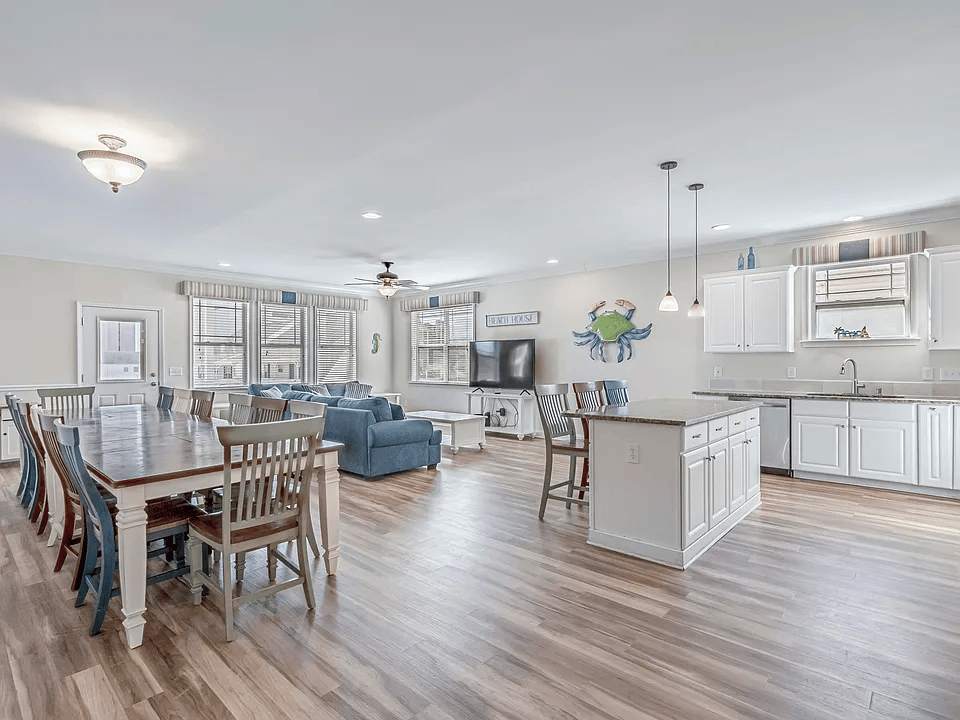 Bright open-concept living, dining, and kitchen area with wood floors, blue sofa, and white cabinets.