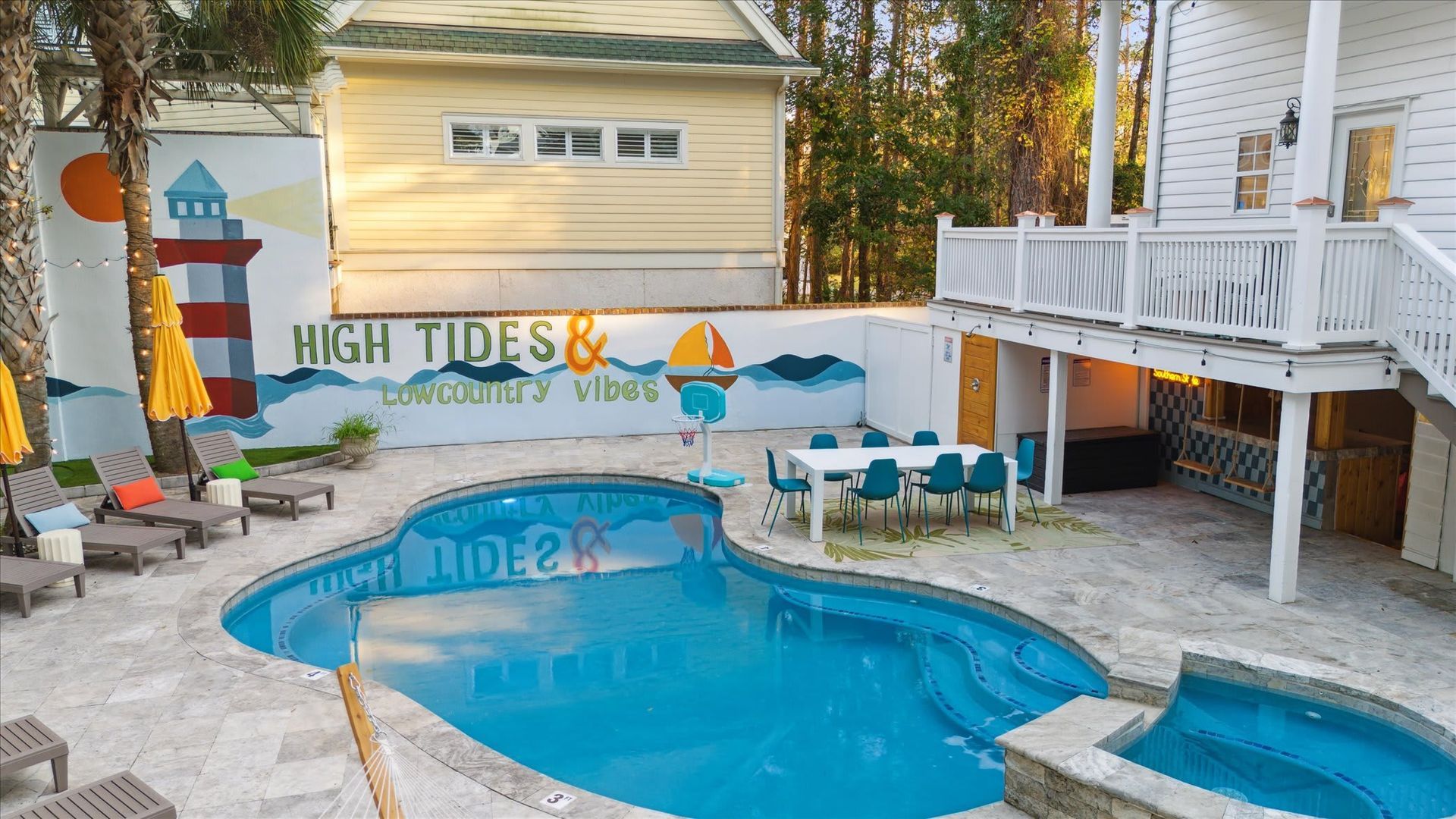 Backyard pool with turquoise water, white deck, striped umbrellas, and mural reading “High Tides, Good Vibes”